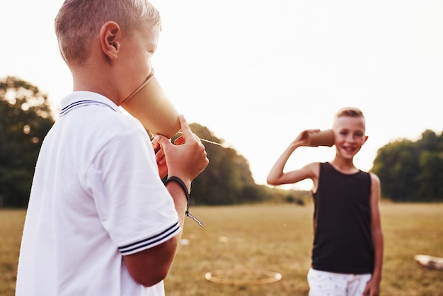 Dos niños se paran en el campo y hablan usando una cuerda por teléfono.