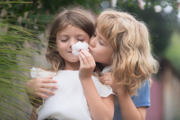 Dos niños pequeños se abrazan y se besan en el jardín de verano Pareja de niños enamorados Niño romántico y niña tímida dando una flor por amor y romance