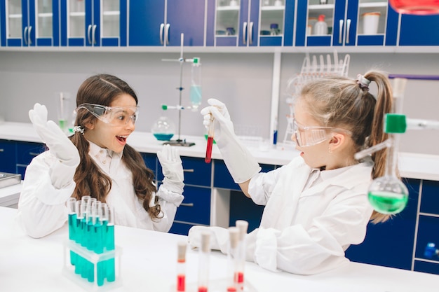 Dos niños pequeños en bata de laboratorio que aprenden química en laboratorio de la escuela. Jóvenes científicos en gafas protectoras haciendo experimentos en laboratorio o gabinete químico. Estudiar ingredientes para experimentos.