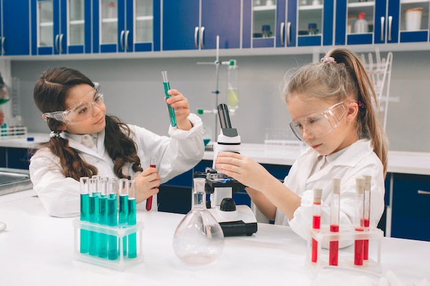 Dos niños pequeños en bata de laboratorio que aprenden química en laboratorio de la escuela. jóvenes científicos en gafas protectoras haciendo experimentos en laboratorio o gabinete químico. estudiar ingredientes para experimentos.