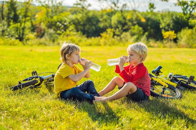 Dos niños pequeños beben agua en el parque después de andar en bicicleta