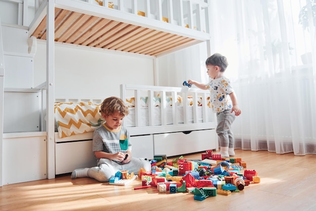 Dos niños pequeños se divierten en el interior del dormitorio con un juego de construcción de plástico