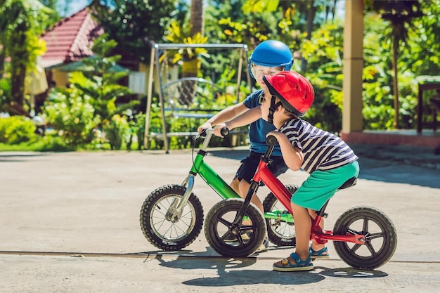 Foto dos niños pequeños divirtiéndose en bicicleta de equilibrio en una carretera tropical del país