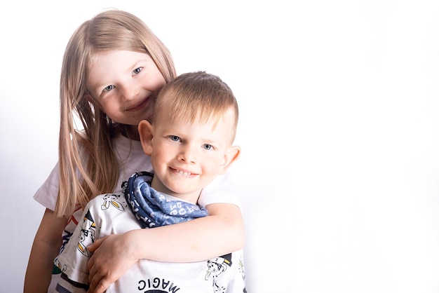 Foto dos niños pequeños felices hermana y hermano sonríen y se abrazan sobre un fondo blanco claro