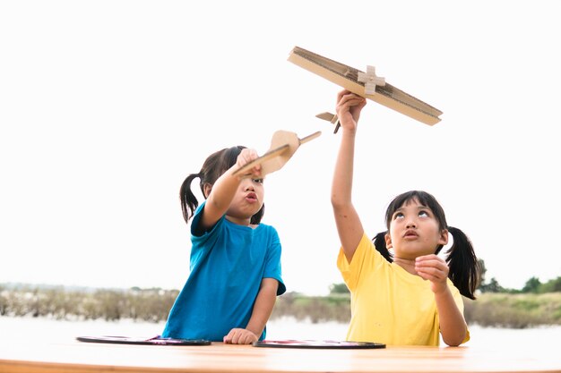 Dos niños pequeños jugando con un avión de juguete de cartón en el parque durante el día.