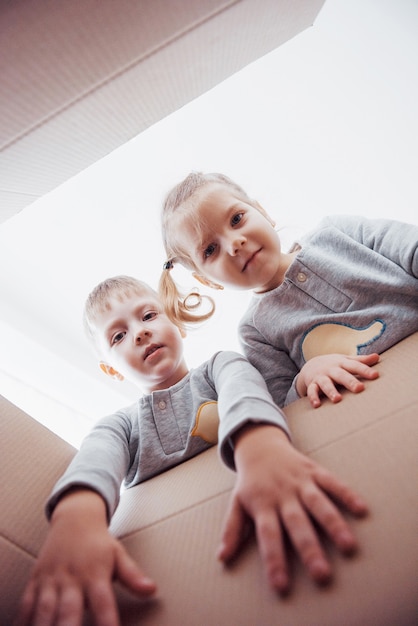 Dos niños pequeños, niño y niña, abriendo una caja de cartón y mirando hacia adentro con sorpresa.