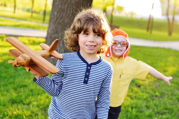 Dos niños pequeños de niños con cabello rizado juegan un avión de juguete de madera en el parque.