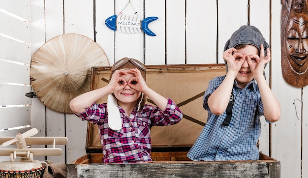 Dos niños pequeños con sombreros de piloto haciendo vasos con las manos.