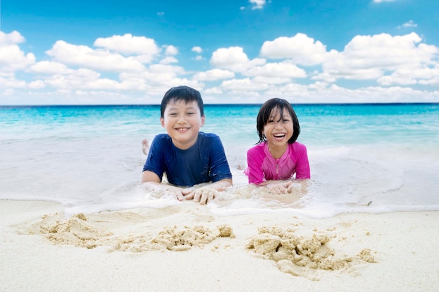 Dos niños pequeños tendidos en la arena.