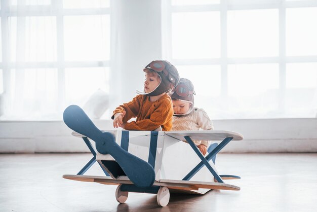 Dos niños pequeños con uniforme de piloto retro divirtiéndose con un avión de juguete en el interior