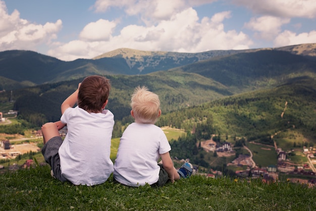 Dos niños sentados en una colina y mirando las montañas.