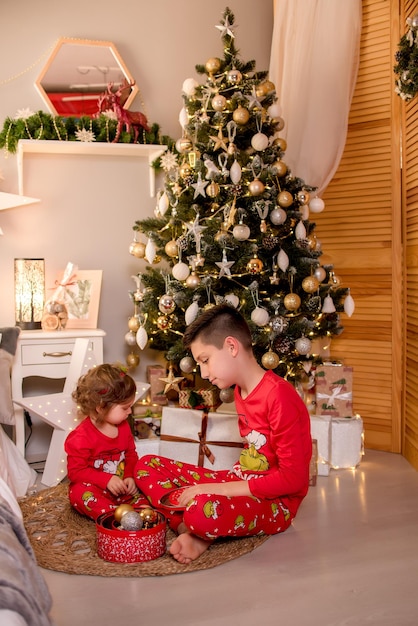 Dos niños se sientan cerca del árbol de Navidad para Navidad y tienen regalos en sus manos.