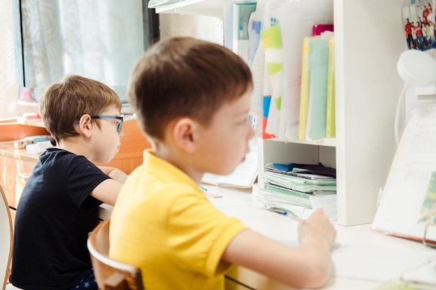 Dos niños se sientan y escriben en cuadernos en la mesa en casa Dos hermanos hacen su tarea Enseñando en casa dos niños