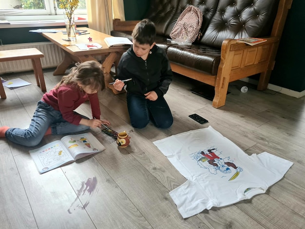 Dos niños se sientan en el suelo y dibujan en camisetas blancas.