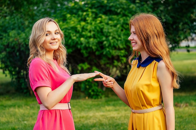 Dos novias activas y alegres, hermosa joven irlandesa pelirroja pelirroja con un vestido amarillo y una mujer rubia europea con un vestido rosa jugando en el parque de verano conociendo a dos amigas