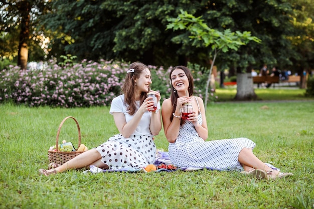 Dos novias de moda con vestidos de lunares haciendo un picnic al aire libre en verano en el parque