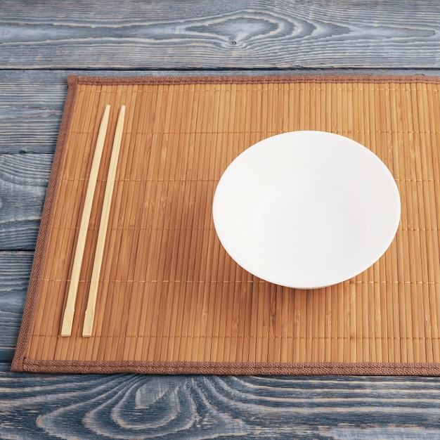 Dos palillos de madera y una taza blanca sobre una estera de bambú