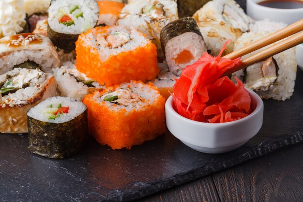 Dos palillos que sostienen el rollo Hosomaki con verduras y diferentes rollos de sushi con mariscos