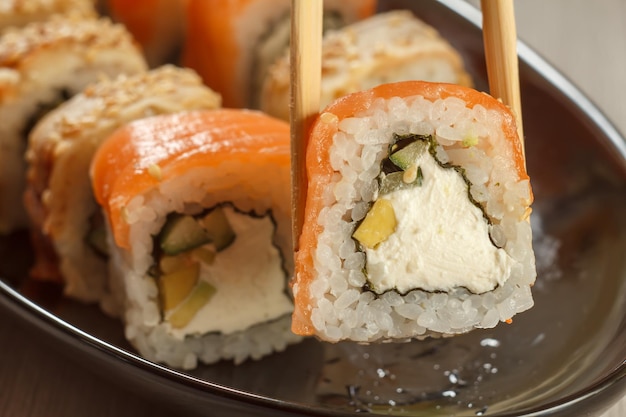 Dos palillos que sostienen Uramaki Philadelphia y diferentes rollos de sushi con mariscos en un plato de cerámica