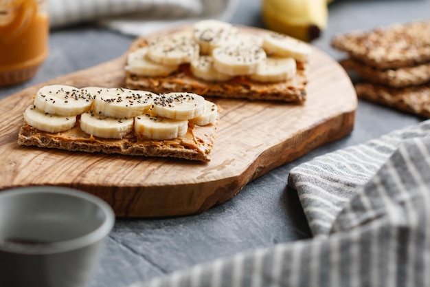 Dos panes multigrano con pasta de maní, rodajas de plátano y semillas de chía en una tabla de madera para servir El concepto de desayuno saludable