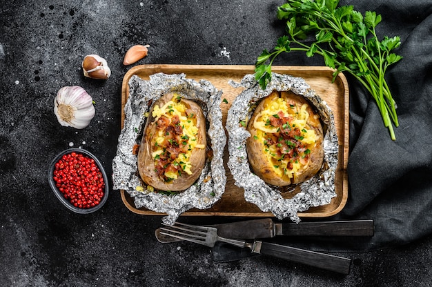 Dos papas al horno con tocino, cebolla verde y queso.