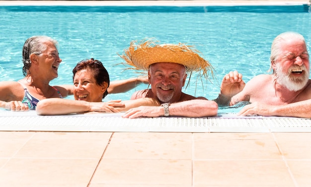 Dos parejas de amigos mayores riéndose disfrutando juntos de la jubilación de vacaciones en la piscina