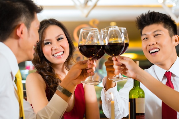 Dos parejas de chinos asiáticos o amigos o gente de negocios brindando durante la cena o el almuerzo en un elegante restaurante con copas de vino tinto