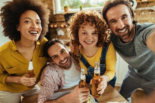 Dos parejas felices bebiendo cerveza y divirtiéndose mientras se toman selfie en casa