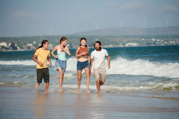 Dos parejas jóvenes felices trotando en la playa soleada por la mañana