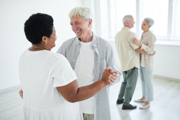 Dos parejas mayores sonriendo el uno al otro cogidos de la mano mientras bailan una danza lenta en el estudio de danza