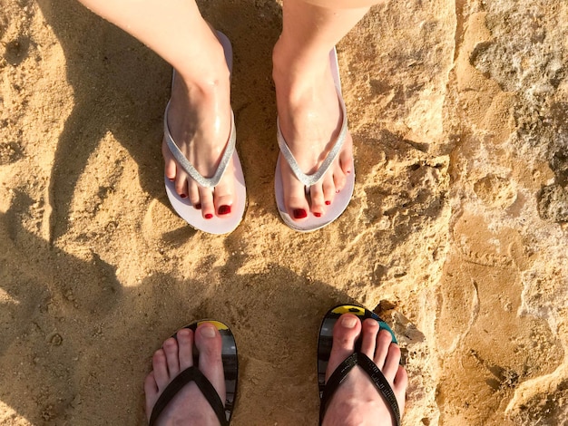 Foto dos pares de piernas masculinas y femeninas con manicura en zapatillas un pie con dedos en chanclas