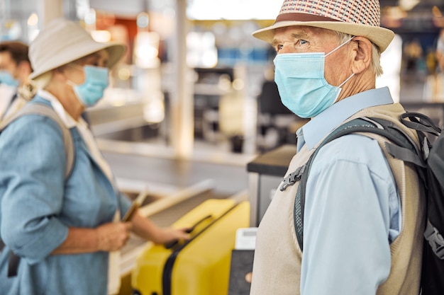 Dos pasajeros con máscaras protectoras colocando su equipaje en la cinta transportadora en el aeropuerto