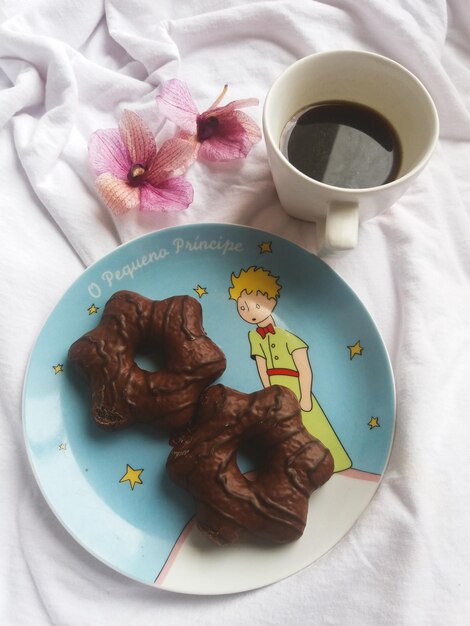 dos pasteles de chocolate y una taza de café al lado de flores rosadas y una hoja blanca en el fondo