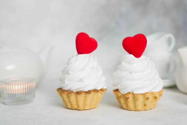 Dos pasteles con corazones rojos y tazas de tetera velas sobre un fondo gris