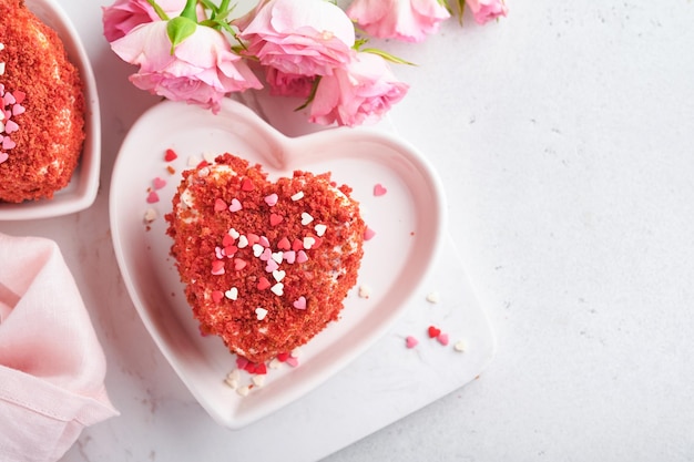 Dos pasteles Terciopelo rojo en forma de corazones en un plato blanco flores rosas y una taza de café en un fondo romántico rosa Idea de postre para el Día de San Valentín Día de la Madre o Día de la Mujer Sabroso postre casero