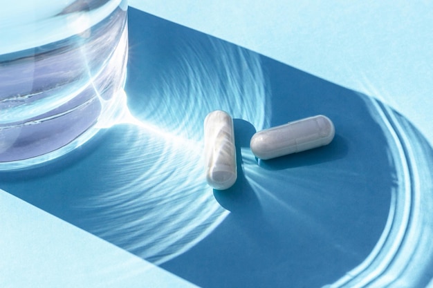 Dos pastillas blancas y un vaso de agua sobre fondo azul Medicina concepto de salud Vista superior Lay Flat