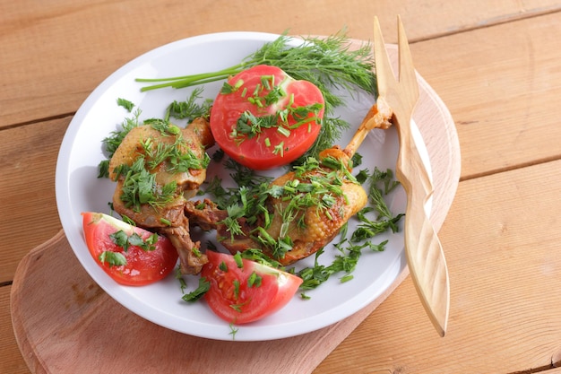 Dos patas de pato doradas con hierbas y tomates en un plato blanco sobre un fondo de madera Primer plano de pato al horno