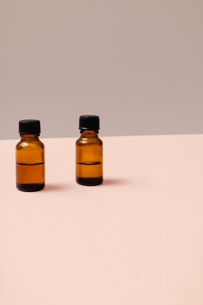 Dos pequeñas botellas de cosméticos de vidrio marrón para productos de belleza sobre un fondo gris y rosa pastel. Composición mínima con espacio de copia. Concepto de bienestar de autocuidado.