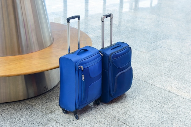 Dos pequeñas maletas azules se encuentran junto a un banco en el salón del aeropuerto.