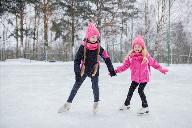 Dos pequeñas muchachas sonrientes que patinan en el hielo en desgaste rosado.