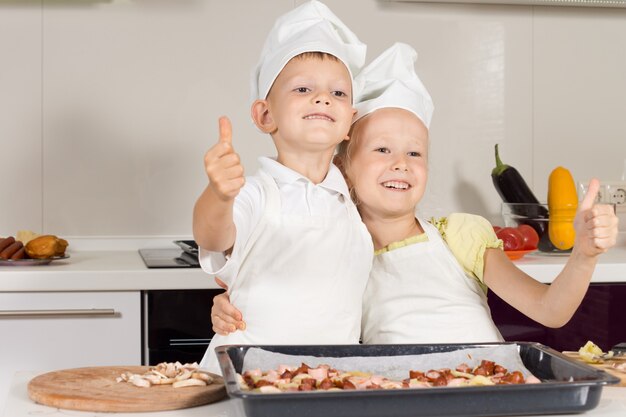Foto dos pequeños chefs mostrando los pulgares para arriba haciendo hincapié en el buen trabajo en hornear pizza.