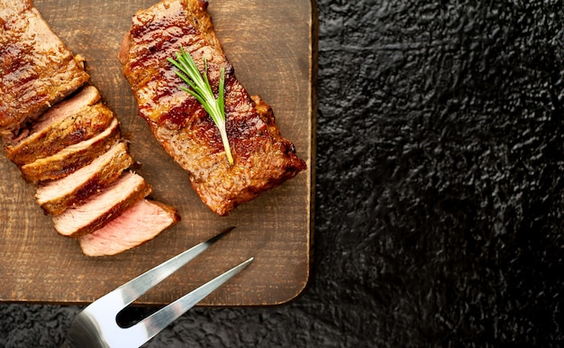 Dos pequeños filetes de res a la parrilla sobre una tabla para cortar con especias sobre un fondo de piedra negra