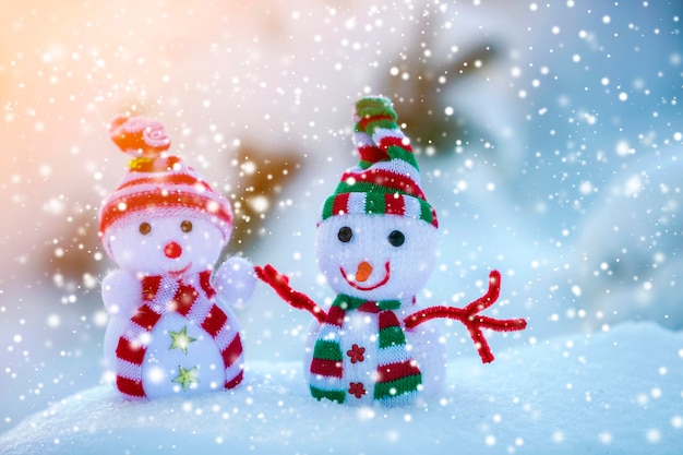 Dos pequeños juguetes divertidos muñeco de nieve bebé en gorros tejidos y bufandas en la nieve profunda al aire libre sobre fondo de espacio de copia azul y blanco brillante. Feliz año nuevo y feliz Navidad tarjeta de felicitación.