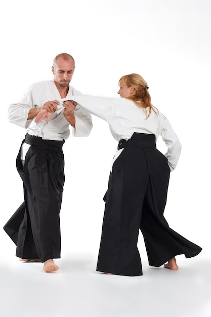 Dos personas, un hombre y una mujer, practican aikido en el tapete aislado de fondo blanco