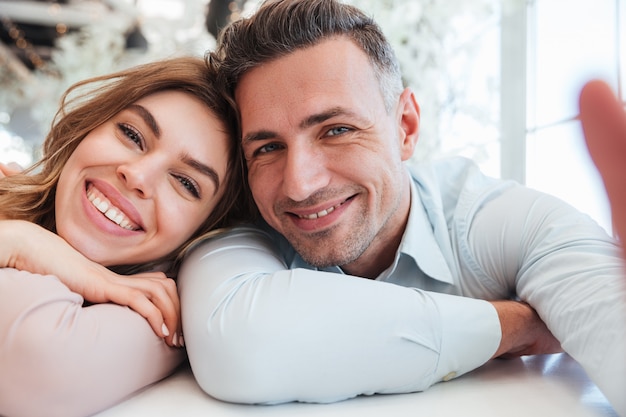 Dos personas lindas, hombre y mujer, divirtiéndose juntos, y haciendo hermosas selfies mientras almuerzan en el restaurante