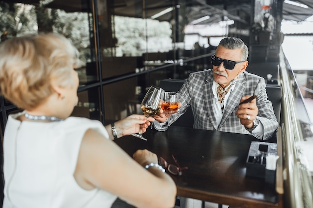 Dos personas mayores encantadoras se sientan en el café moderno y prueban el vino