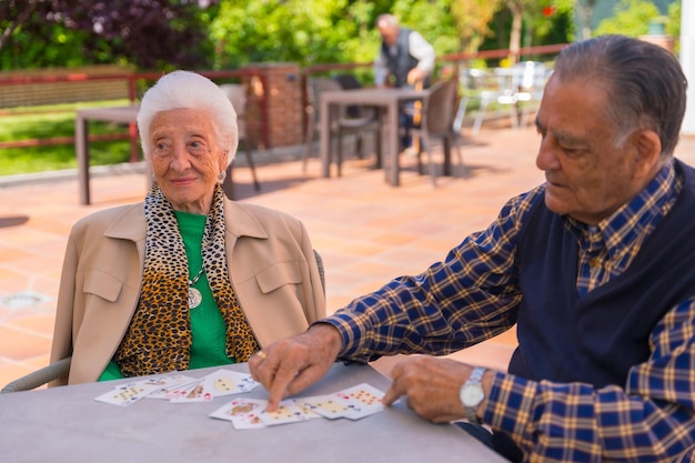 Foto dos personas mayores en el jardín de un hogar de ancianos o de retiro jugando a las cartas en una mañana de verano