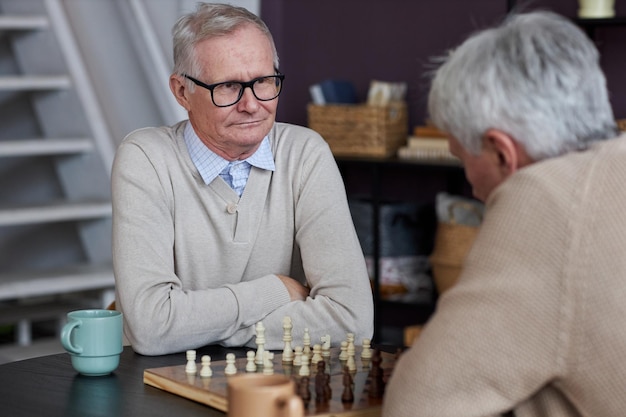 Dos personas mayores jugando al ajedrez en el área de la sala común en la casa de retiro