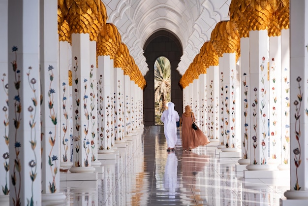 Dos personas en ropa árabe caminando en la Gran Mezquita Sheikh Zayed en Abu Dhabi, Emiratos Árabes Unidos