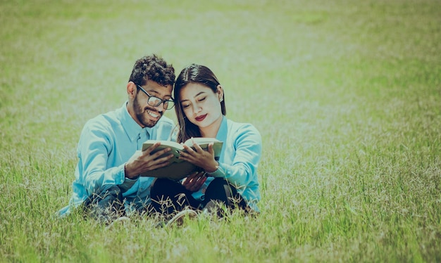 Dos personas sentadas en el césped leyendo un libro concepto de personas leyendo afuera Una pareja sentada en el césped leyendo un libro